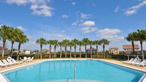 Une piscine entourée de chaises longues, de palmiers et de maisons en arrière-plan.