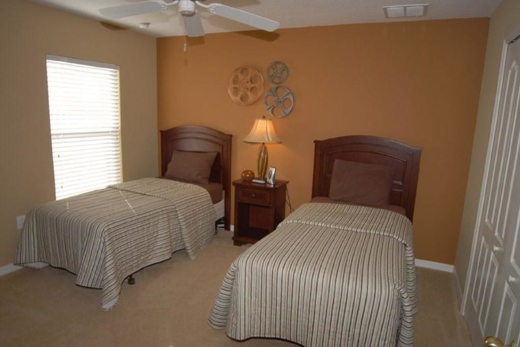 A bedroom with two single beds, a ceiling fan, and a nightstand with a lamp.
