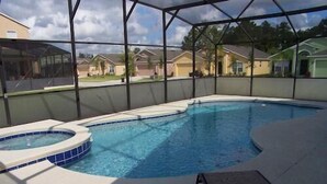 A swimming pool with a hot tub, surrounded by a covered area with a view of houses in the background.