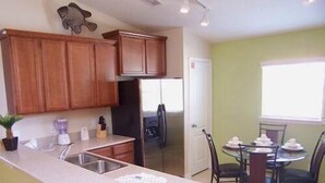 A kitchen with wooden cabinets, a refrigerator, a sink, and a dining area with a table and chairs.