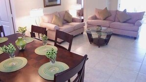 A living room with two sofas, a glass coffee table, and a dining table with placemats.
