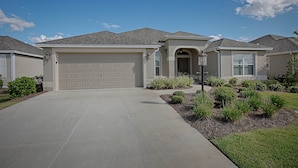 A residential house with a garage, a driveway, and landscaped garden. - Rabbit Run Path Home 3 Bedroom by The VIR Group (Wildwood)