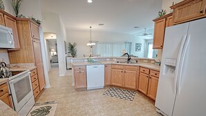 A modern kitchen with wooden cabinets, a white refrigerator, a dishwasher, and a large island with a sink. - Rabbit Run Path Home 3 Bedroom by The VIR Group (Wildwood)