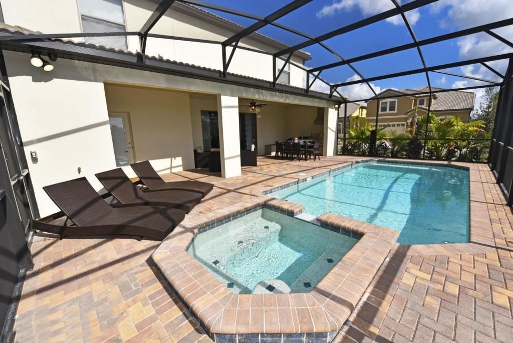 A swimming pool with a hot tub, lounge chairs, and a covered patio area.
