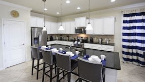 Una cocina moderna con armarios blancos, electrodomésticos de acero inoxidable e iluminación colgante.