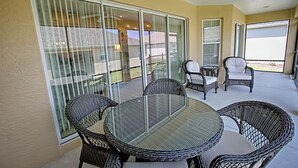 Un patio couvert avec une table ronde en verre et des chaises en osier, de grandes portes-fenêtres coulissantes et un ventilateur de plafond.