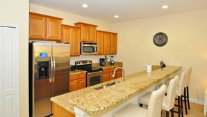 A kitchen with wooden cabinets, stainless steel appliances, a granite countertop, and a clock on the wall. - 8939 Paraside Palms Townhome 4 Bedroom by Florida Star (Kissimmee)