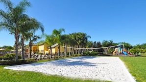 A beach volleyball court with a net, palm trees, and a colorful playground in the background. - 8939 Paraside Palms Townhome 4 Bedroom by Florida Star (Kissimmee)