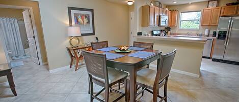 A modern kitchen with wooden cabinets, a stainless steel refrigerator, and a dining area with a table and chairs.