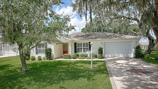 A single-story house with a red door, a garage, and a well-maintained lawn. - Ansel Avenue Home 2 Bedroom by The VIR Group (The Villages)