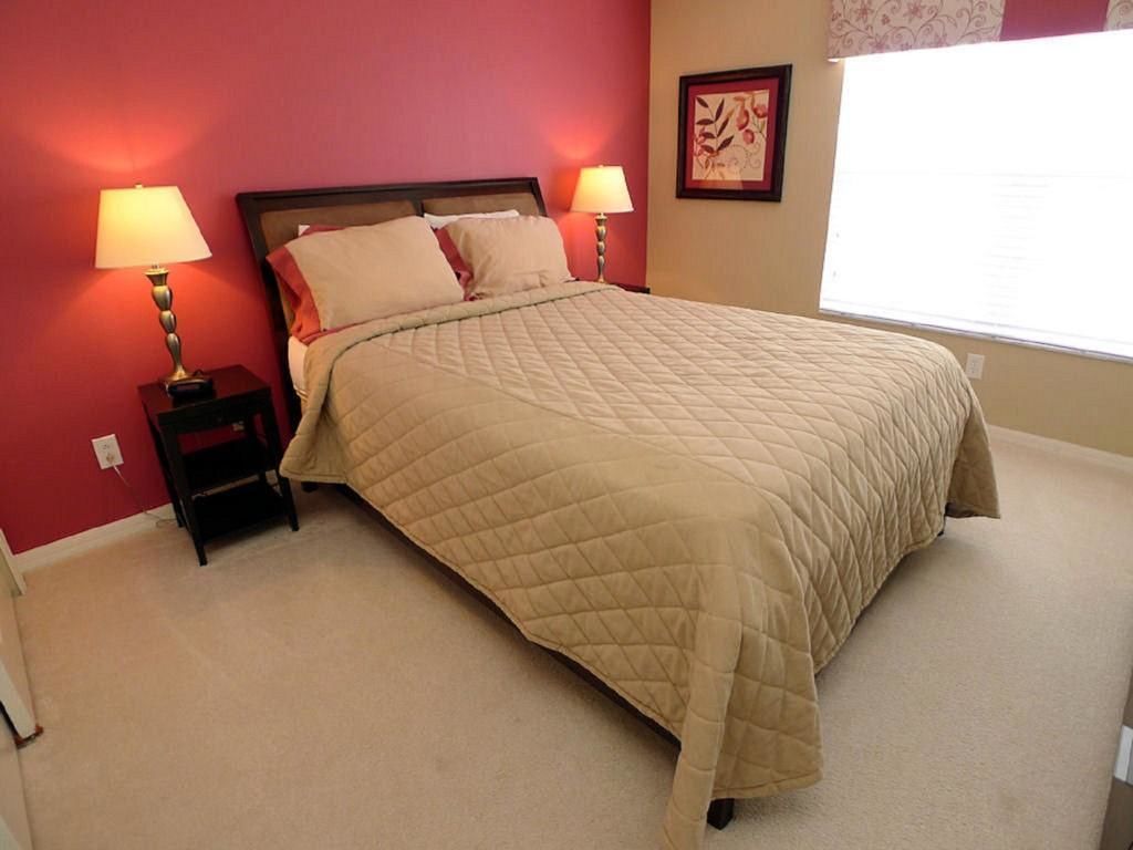 A bedroom with a bed, two bedside lamps, a nightstand, a framed picture on the wall, and a window.