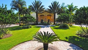 A well-maintained garden with a central pathway leading to a building with a yellow facade and arched entrance. - 8981 Paradise Palms Townhome 5 Bedroom by Florida Star (Kissimmee)