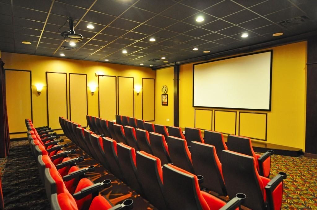 A movie theater with rows of red and black seats, a large screen, and yellow walls.