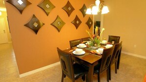 Un coin repas avec un mur brun, un lustre et une table dressée pour six personnes.