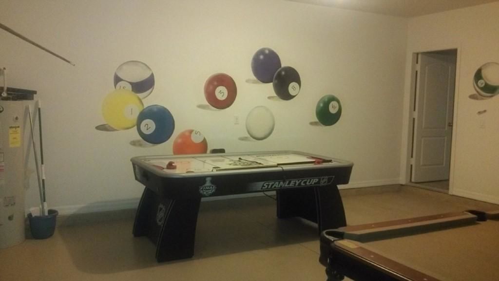 Una mesa de billar con la etiqueta 'STANLEY CUP', una pared con bolas de billar numeradas, una puerta y un basurero.