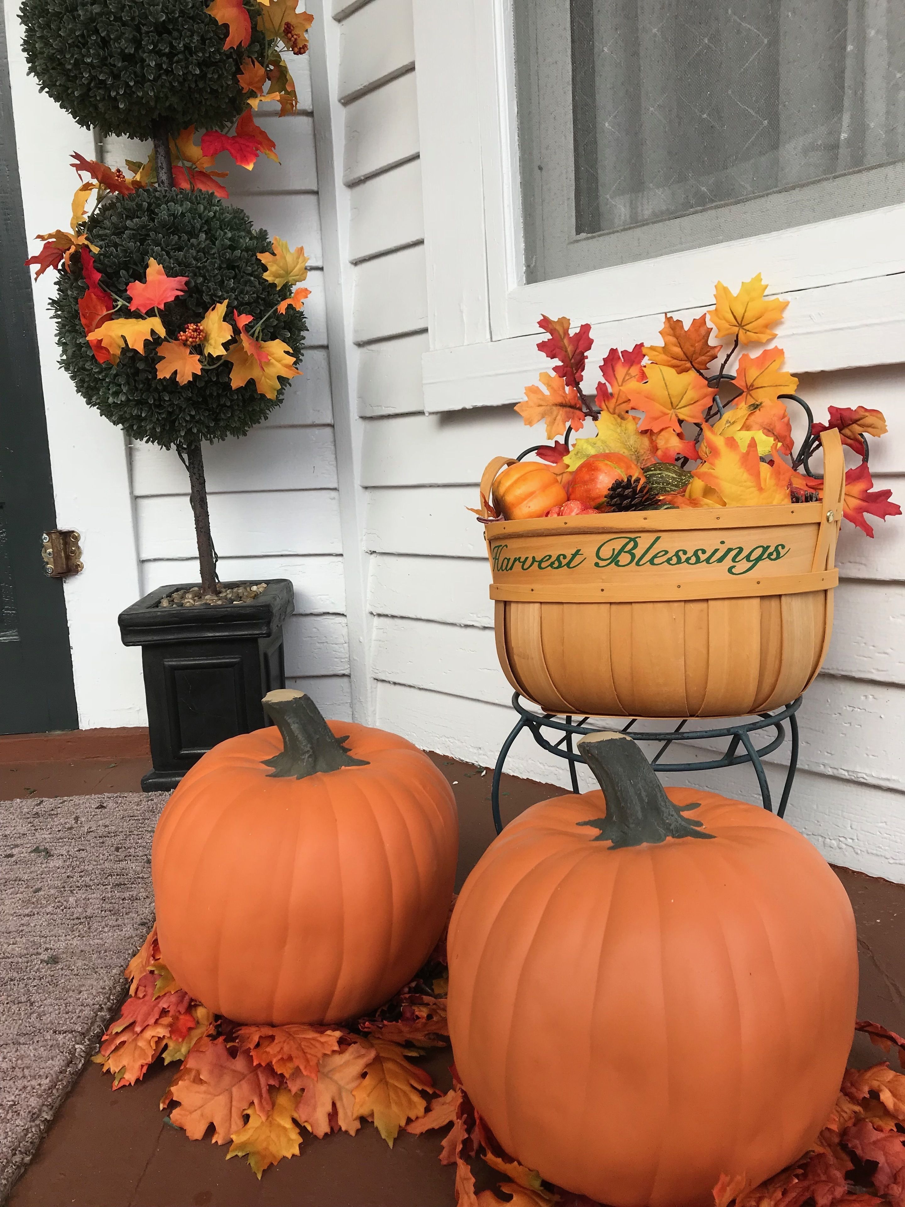 Un porche con dos calabazas y una maceta decorativa con hojas otoñales y un letrero que dice "Harvest Blessings".