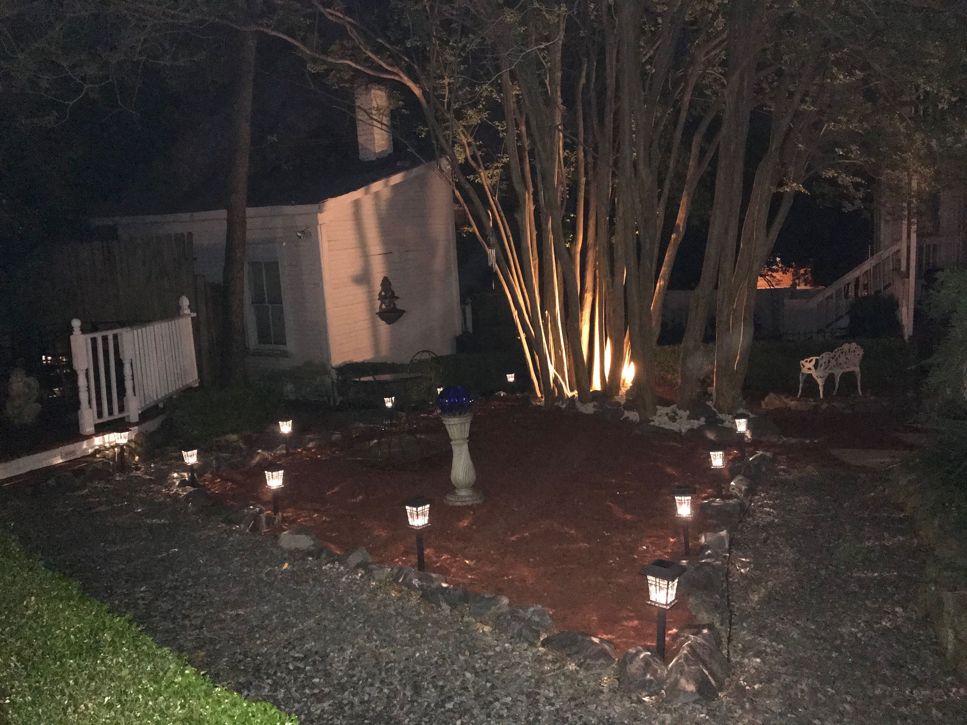 A nighttime outdoor area with a paved surface, surrounded by trees and a white fence.