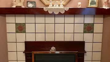 Une cheminée avec un manteau orné de carreaux, un tableau encadré au-dessus, et deux appliques murales.