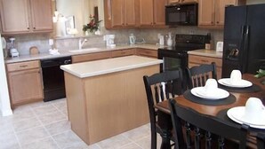 A kitchen with wooden cabinets, a black refrigerator, a dining table with chairs, and a small island. - 956 Watersong House 6 Bedroom by Florida Star (Davenport)