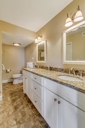 A bathroom with a double sink, two mirrors, and a toilet.