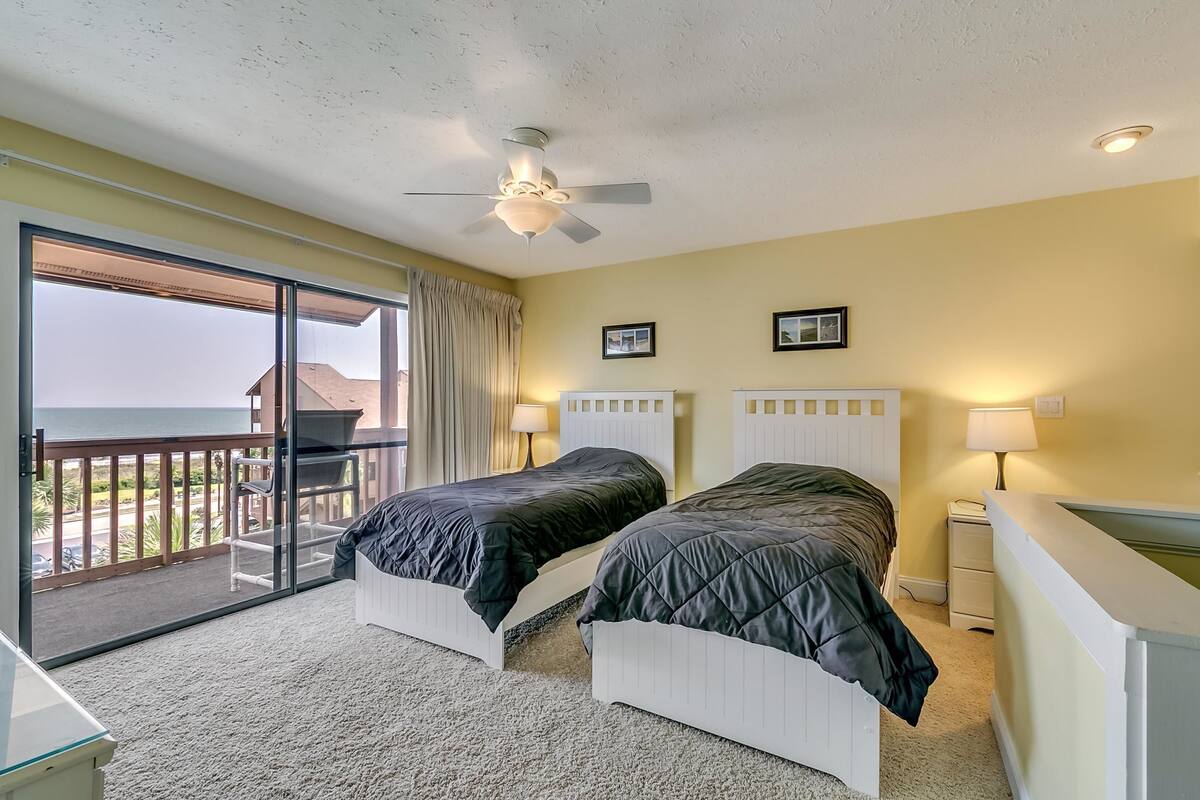 A bedroom with two beds, a ceiling fan, and a view of the outdoors.