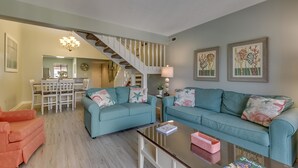 Un salon avec des canapés de couleur turquoise, une table basse et un escalier menant à un espace repas.