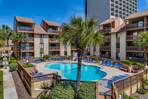A hotel with a central swimming pool surrounded by lounge chairs and palm trees. - Anchorage Abode I A02 2 Bedroom Condo by Anchorage (Myrtle Beach)