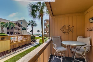 A balcony with a view of a pool and palm trees, a white table and two chairs, and a wall with a fish decoration. - Anchorage Abode I A02 2 Bedroom Condo by Anchorage (Myrtle Beach)