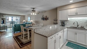 A modern kitchen with white cabinets, a granite countertop, and a dining area with a table and chairs. - Anchorage Abode I A02 2 Bedroom Condo by Anchorage (Myrtle Beach)