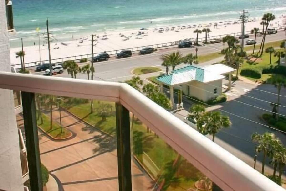 Ein Balkon mit Blick auf einen Strand, einen Parkplatz und ein kleines Gebäude.