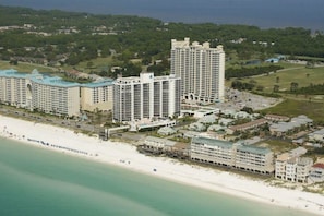 Ett hotellkomplex vid kusten med flera höga byggnader, en strand och omgivande grönska.