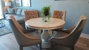 Una mesa redonda de comedor con cuatro sillas tapizadas, una planta en maceta y una pared de color claro.