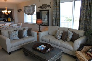A living room with two grey sofas, a coffee table, and a chandelier. There is a window with curtains and a view of the outdoors.