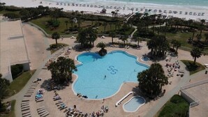 An aerial view of a resort with a large central pool, multiple smaller pools, and a beach area with umbrellas and lounge chairs. - St Croix at Silver Shells 3 Bedroom Apartment by BnD (Destin)