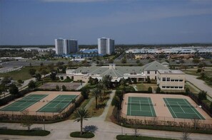 Un grand bâtiment doté de plusieurs courts de tennis, entouré de verdure et situé à proximité d’immeubles de grande hauteur.