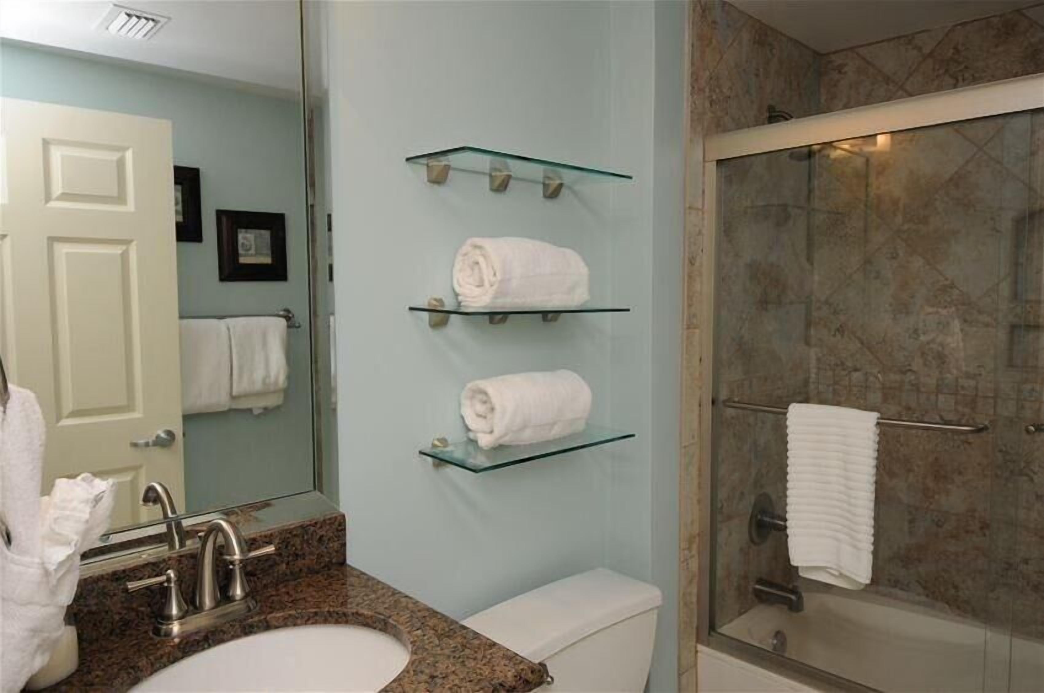 A bathroom with a granite countertop sink, a white toilet, and a glass shower enclosure.