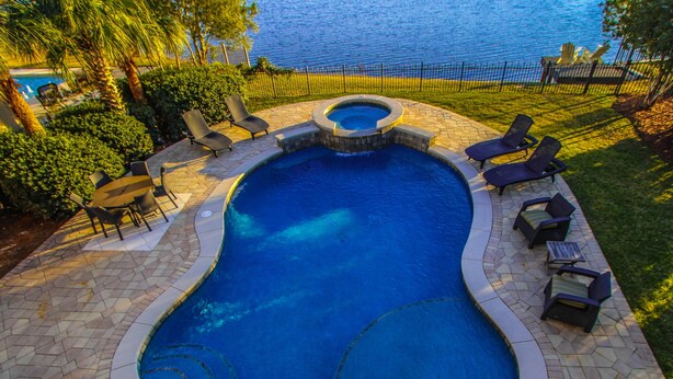 Una piscina con jacuzzi, rodeada de sillones de descanso y un patio de piedra.