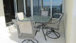 A glass-top table with four chairs, a sliding glass door, and a view of the ocean.