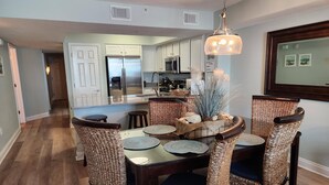 A dining area with wicker chairs, a round table, and a hanging light fixture. - 3rd Floor SeaDunes 3 Bedroom Apartment by BnD (Fort Walton Beach)
