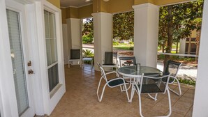 A covered patio with a round table and chairs, a television, and a door leading to the interior.