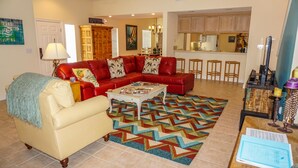 A living room with a red sofa, a beige armchair, and a coffee table. There is a colorful rug on the floor.