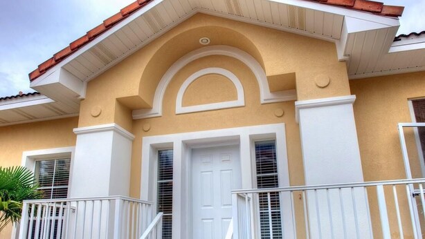 A two-story house with a beige facade, white trim, and a red-tiled roof.