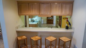 A kitchen with wooden cabinets, a white countertop, and four woven stools.