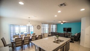 A modern kitchen with a central island, dining area with chairs, and a living room with a TV.
