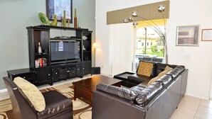 A living room with a black entertainment unit, leather sofa, and a coffee table. - 101 Aviana House 6 Bedroom by Florida Star (Davenport)