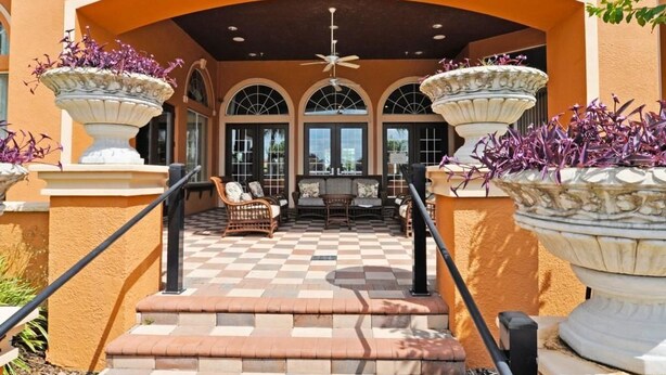 A covered outdoor seating area with a checkered floor, a ceiling fan, and large planters with purple flowers. - 101 Aviana House 6 Bedroom by Florida Star (Davenport)