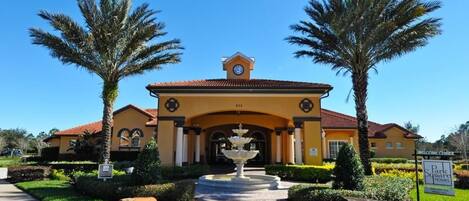 A yellow building with a clock tower, palm trees, and a fountain in the center.