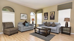A living room with two sofas, a coffee table, and a striped armchair. There are two lamps on side tables and framed artwork on the walls. - 112 Watersong House 6 Bedroom by Florida Star (Davenport)