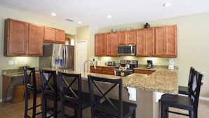 A kitchen with wooden cabinets, a stainless steel refrigerator, a microwave, and a coffee maker. - 112 Watersong House 6 Bedroom by Florida Star (Davenport)