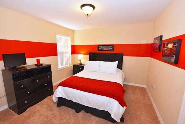 A bedroom with a bed, a TV on a dresser, a nightstand with a lamp, and a window with blinds. - 1127 Cypress House 6 Bedroom by Florida Star (Davenport)